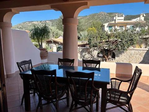 Un tavolo da pranzo per sei su una terrazza coperta, con le colline dietro